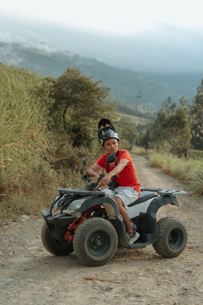 Young boy on ATV on a dirt road in Cáqueza, Colombia with scenic landscape.