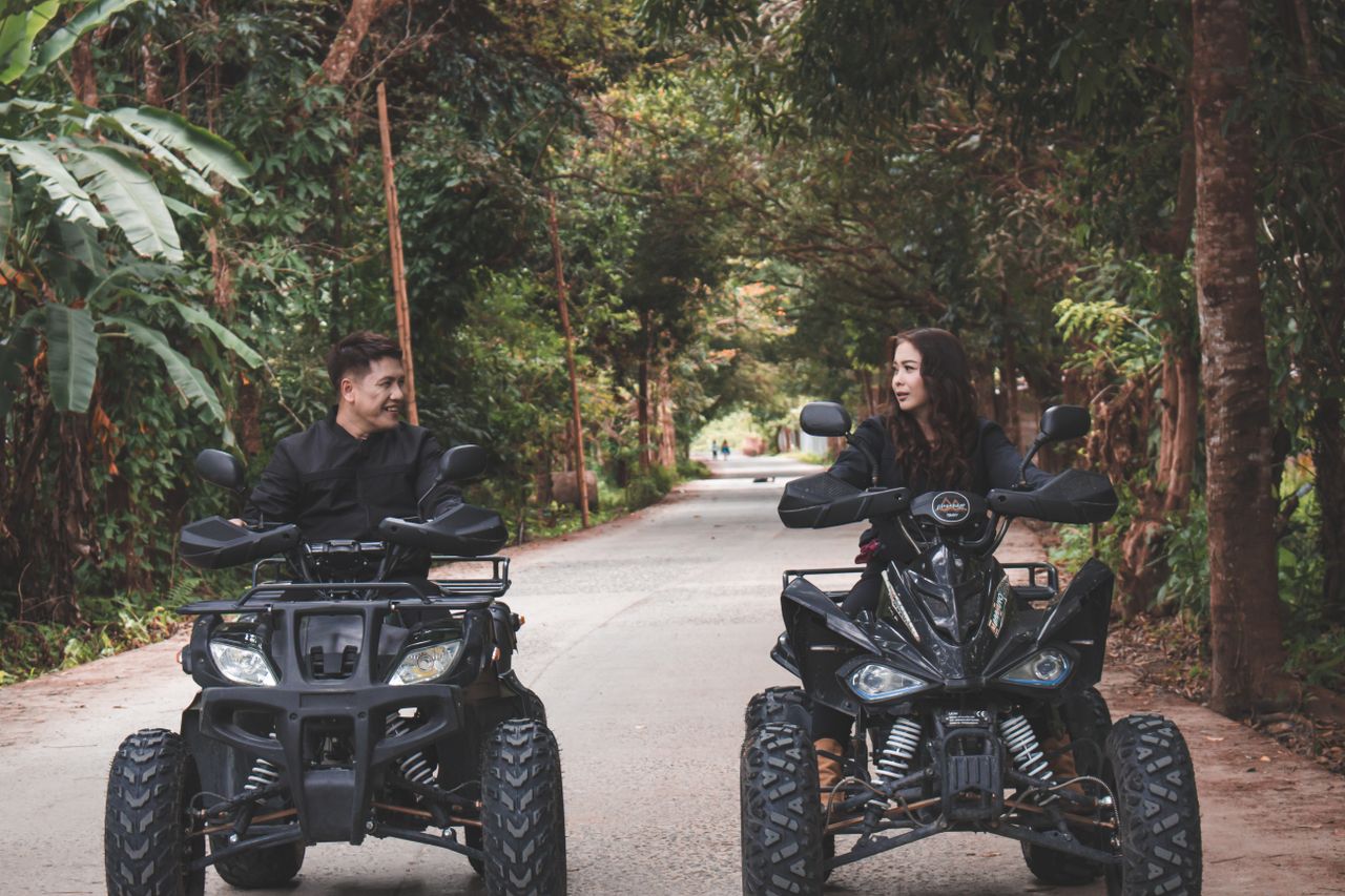 hero-img-02 A couple enjoying a scenic ride on quad bikes through a lush green path.