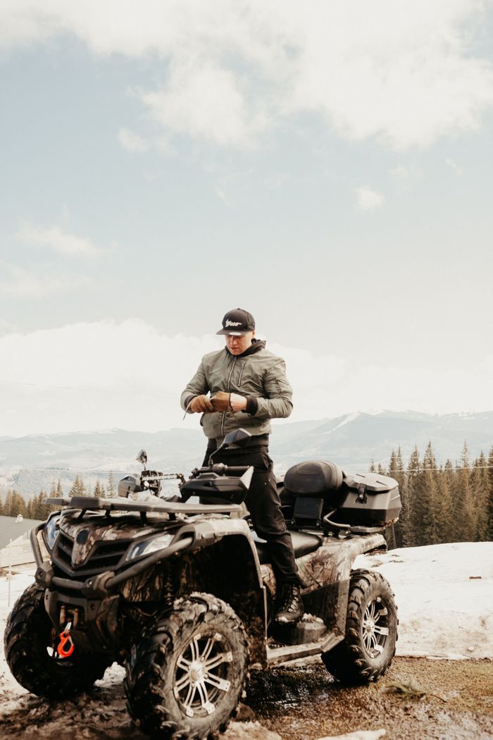 gallery-6 Man enjoying a winter adventure on ATV in snowy mountainous landscape.