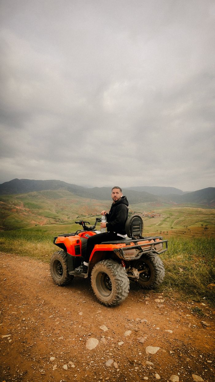 Man on an ATV enjoying a scenic ride through a mountainous landscape under a cloudy sky.
