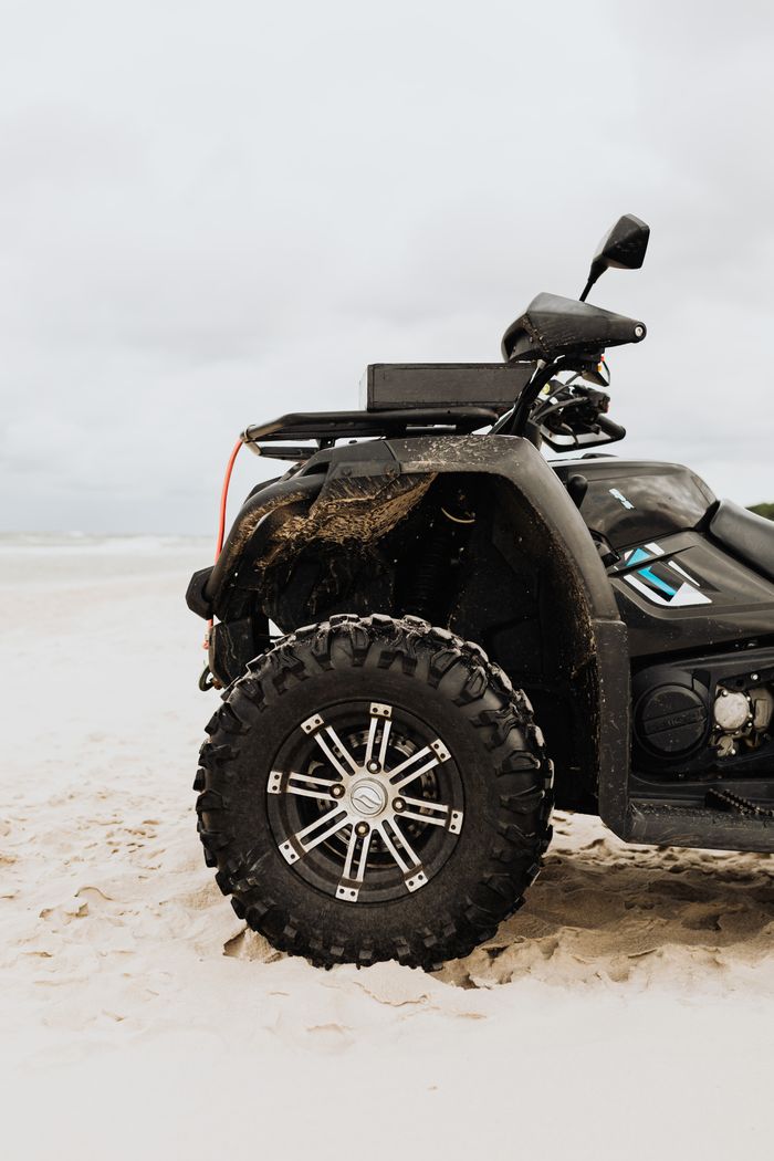 gallery-3 Close-up of a rugged all-terrain vehicle on a sandy beach with cloudy skies.